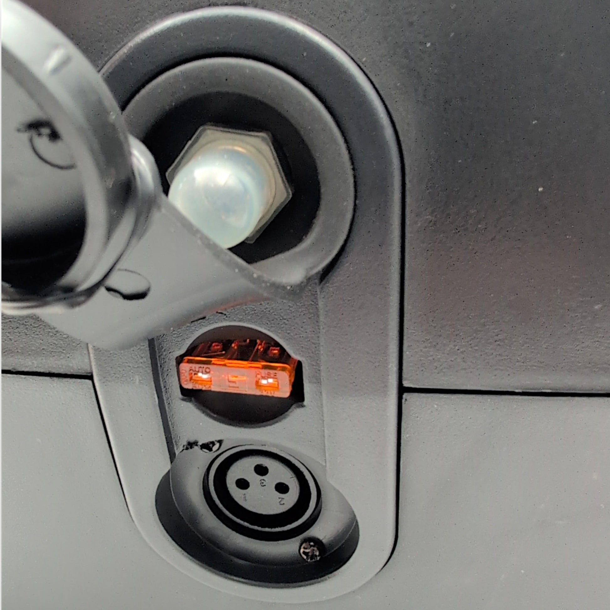 Cover lifted off of the front port. Shows the 3-pin XLR charging port, a 5 Amp Fuse, and the reset switch for the circuit breaker